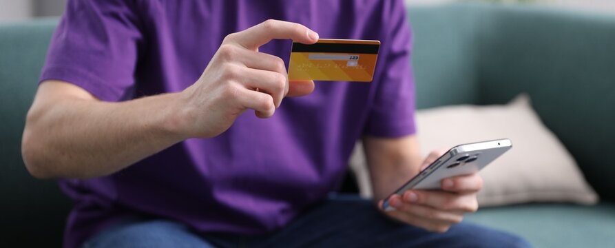 Young man making online payment with phone and credit card indoors, closeup