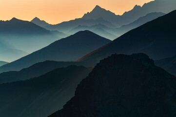 Aerial view of the majestic Tri Kopy peak layered in shades of blue and grey, fading into the horizon under a soft orange sky., Ziar, Zilina Region, Slovakia.