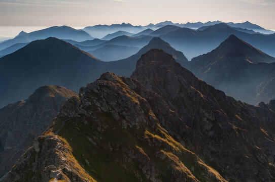 Aerial view of the rugged, sun-kissed peaks of Tri Kopy contrasted against the ethereal, misty blues of distant mountains, Ziar, Zilina Region, Slovakia.