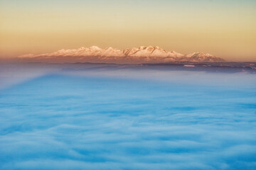 Aerial view of snow-capped peaks pierce through a soft blanket of ethereal clouds, a serene landscape of contrasting textures and tones, Spisska nova Ves, Kosicky kraj, Slovakia.