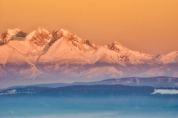Aerial view of snow-capped peaks pierce the golden sky, casting long shadows over the rugged landscape, a serene scene of winter's embrace, Spisska nova Ves, Kosicky kraj, Slovakia.
