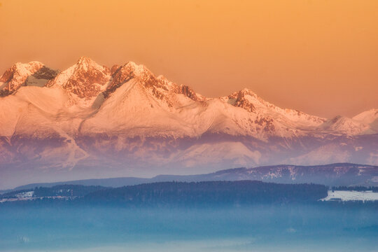 Aerial view of snow-capped peaks pierce the golden sky, casting long shadows over the rugged landscape, a serene scene of winter's embrace, Spisska nova Ves, Kosicky kraj, Slovakia.