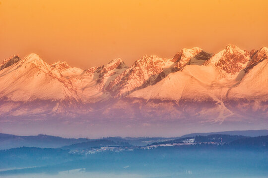 Aerial view of snow-capped peaks touched by the warm glow of sunset, creating a stunning contrast with the cool blue shadows in the valleys below, Spisska nova Ves, Kosicky kraj, Slovakia.