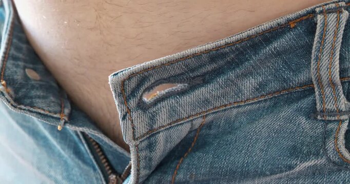 Trying on clothes in fitting room. Skinny jeans and a fat belly. Man was unable to button his jeans at the waist. Close-up of blue jeans and paunch, beer belly. The pants size is small and unsuitable