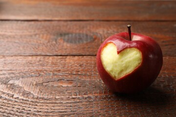 Ripe apple with carved heart on wooden table, closeup. Space for text