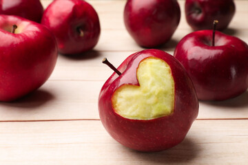 Ripe apple with carved heart and whole ones on light wooden table, closeup