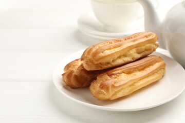 Tasty eclairs served on white wooden table, closeup. Space for text