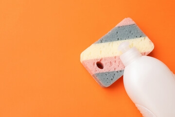 Kitchen sponge and dish soap on orange background, top view. Space for text