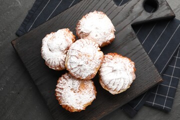 Tasty profiteroles with powdered sugar on black table, top view