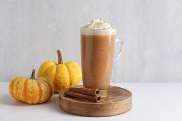 Delicious pumpkin latte with whipped cream, cinnamon sticks and fresh vegetables on white table near grey wall, closeup