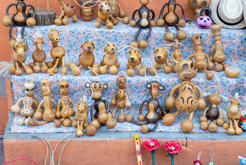 Display of handmade gourd animal figures including dogs, monkeys, horses, and skull decorations on a shelf with floral fabric