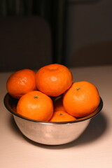 Vertical composition: metal bowl with tangerines on a light table, top view slightly from side, vibrant fruits, minimalist background