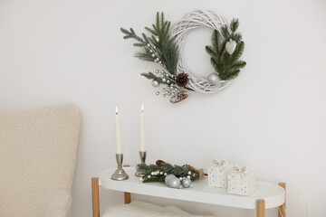 Christmas decor and burning candles on console table near white wall indoors. Interior design