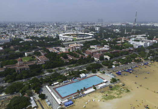 Aerial view of the vibrant contrast between the serene blue pool and the golden sands near Marina Beach, with the stadium in the distance, Chennai, Tamil Nadu, India.