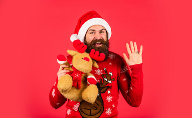 I wish. ready for xmas gifts and presents. new year shopping discounts. mature man with reindeer toy red background. Christmas party time. bearded santa claus in hat. celebrate the party