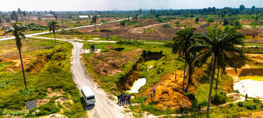 Aerial view of a landscape where scars of excavation meet the vibrant green of nature, with a group of people gathered near a bus, Ogale, Eleme, Rivers State, Nigeria
