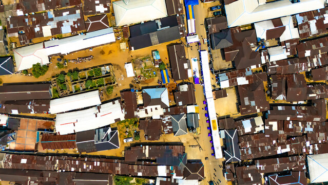 Aerial view of rooftops interlock like puzzle pieces, punctuated by vibrant blue awnings along the road, creating a striking contrast, Mgboshimini, Port Harcourt, Rivers State, Nigeria.