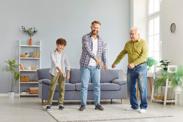Funny dancing playful family of three generation men, senior grandfather, adult father, small child grandson dance together, making fun on weekend celebrating father's day holiday entertainment joy