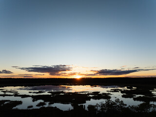 Aerial drone view of the Seli Bog wetlands in Estonia featuring a dramatic sunset reflecting in dark peat pools