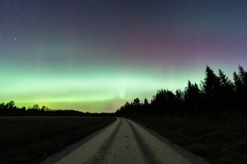 Green Aurora Borealis Northern Lights illuminating the starry night sky over a rural gravel road in the Estonian countryside