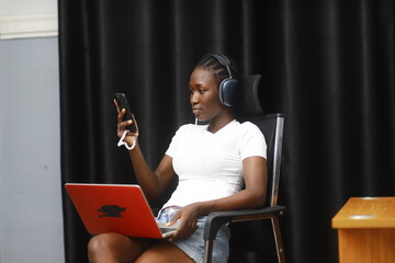 Young African lady using laptop. Woman working on computer using phone
