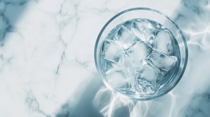 Overhead shot of a glass filled with ice cubes on a marble surface, capturing the play of light and shadow, creating a refreshing and cool vibe