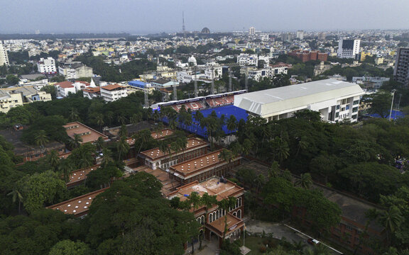 Aerial view of a vibrant cityscape where colonial red-roofed buildings nestle among lush green canopies, contrasted by modern structures, Chennai, Tamil Nadu, India.