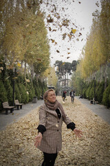 Fototapeta premium A woman throws autumn leaves into the air in a park in Tehran, the capital of Iran