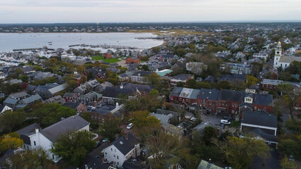 Aerial view of quaint rooftops nestled among verdant trees leading to the tranquil harbor waters, a serene tapestry under the vast sky, Nantucket, Massachusetts, United States.