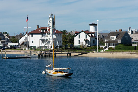 Aerial view of Brant Point Lighthouse watching over a sailboat in calm waters, a beacon of maritime history against the backdrop of charming coastal homes, Nantucket, Massachusetts, United States.