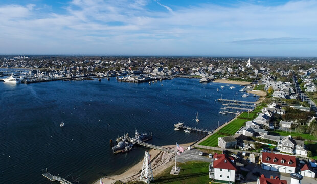 Aerial view of the serene harbor waters reflecting the sky's azure hues, while the iconic Brant Point Lighthouse stands sentinel against the soft sandy beach, Nantucket, Massachusetts, United States.