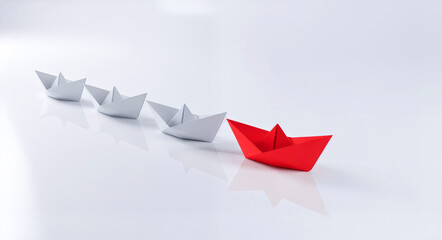 Red origami boat leading a group of white boats on a clean reflective surface, symbolizing leadership, direction, and standing out from the crowd