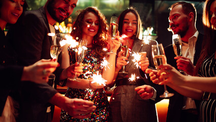 Friends gather at a vibrant bar to celebrate New Year's Eve. They enjoy drinks while holding...