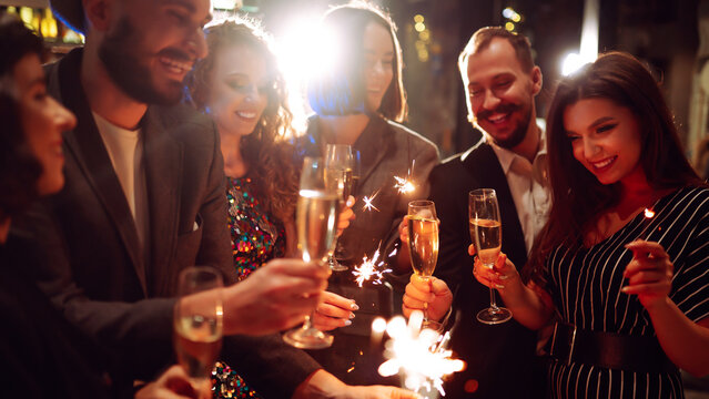 Friends gather at a vibrant bar to celebrate New Year's Eve. They enjoy drinks while holding sparklers, surrounded by a festive atmosphere and sparkling decorations.