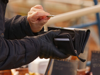 A shopper in a winter jacket and gloves takes coins from a wallet while making a purchase at a...