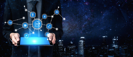 A businessman elegantly displays a tablet loaded with digital icons, symbolizing innovation and connectivity against a dazzling night skyline, representing modern technology in business. Tessel