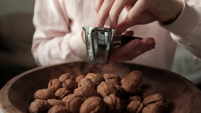 Closeup video of cracking walnuts using special tool. Nuts in a vintage wooden bowl. Healthy snack rich in fiber, fat and nutrients. Removing shell from walnuts. 