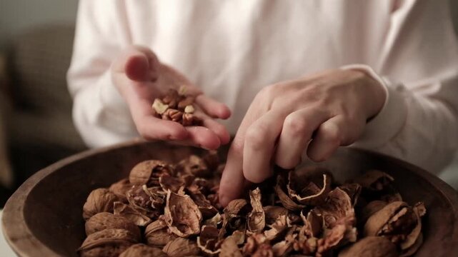 Closeup video of cracking walnuts using special tool. Nuts in a vintage wooden bowl. Healthy snack rich in fiber, fat and nutrients. Removing shell from walnuts. 