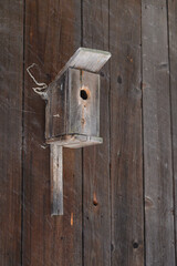 Old wooden birdhouse mounted on wooden boards of a barn.