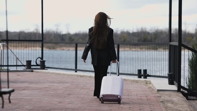 A woman carrying a pink suitcase walks along a patterned sidewalk, demonstrating the suitcase's design and functionality. Travel concept.