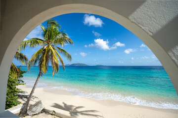 Beautiful tropical white sand beach and crystal clear turquoise waters of Apple Bay on Tortola framed by a coconut palm tree and an arched balcony