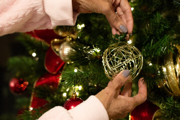 Hands Hanging Christmas Ornaments on Tree. Placing Decoration on Christmas Tree at Home.