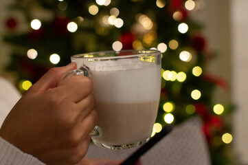 Cup of Hot Beverage With Christmas Lights in Background. Woman Holding a Mug in a Festive Living Room
