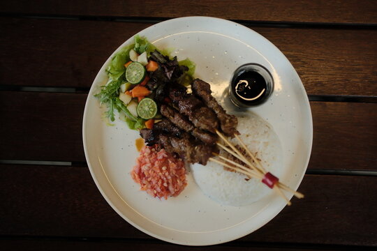 Delicious Indonesian satay skewers served with rice, vibrant salad, and spicy sambal on a modern plate perfect for food blogs and restaurant menus