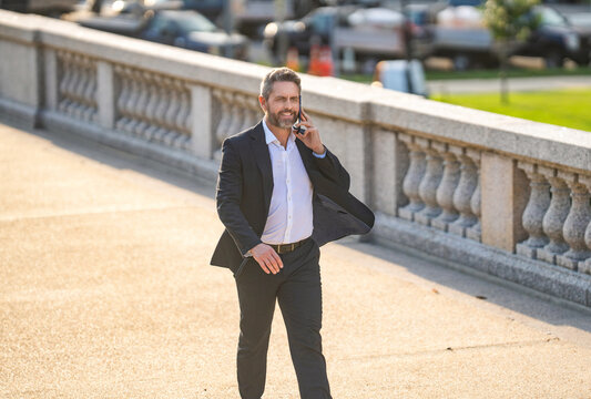 Business man walking and talking on phone outdoor. Businessman negotiation online. Man phone conversation in suit. Mature Hispanic business man with phone. Business communication of businessman - Powered by Adobe