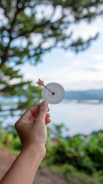 Hand holding paper target with arrow in focus against blurred lake and tree background expressing achievement and hope