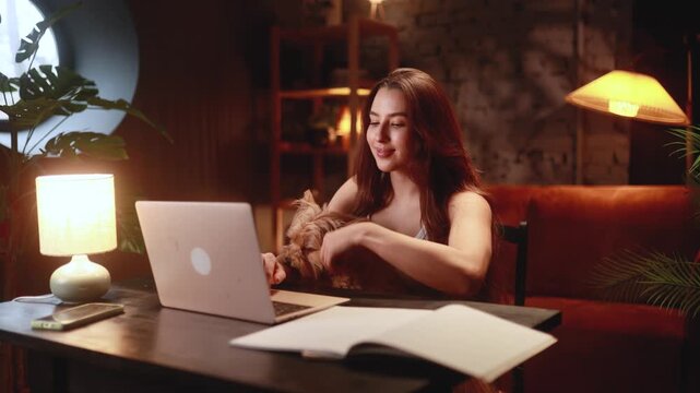 caucasian learner reviews material alongside furry friend, evening scene of student studying with pet close by, quiet nighttime study setup featuring student and their loyal dog beside laptop