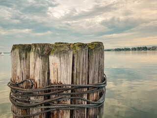 Old Wooden Bollard Posts Tied in Nautical Ropes at the End of a Pier. Thick rustic wooden bollard posts are wrapped in black nautical style ropes. Located on Lake Michigan in Northern Michigan, USA.
