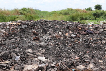 Burned waste pile covering ground with dark ash and scattered debris everywhere