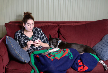 Young woman relaxing on a sofa, looking at her cell phone, with her sleeping dog